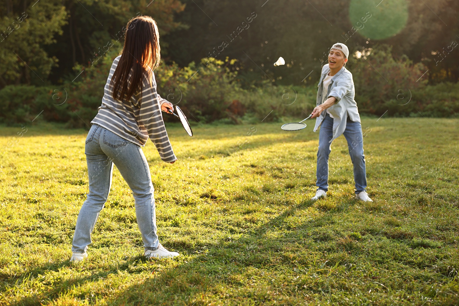 Photo of Young man and woman playing badminton in park on sunny day, selective focus