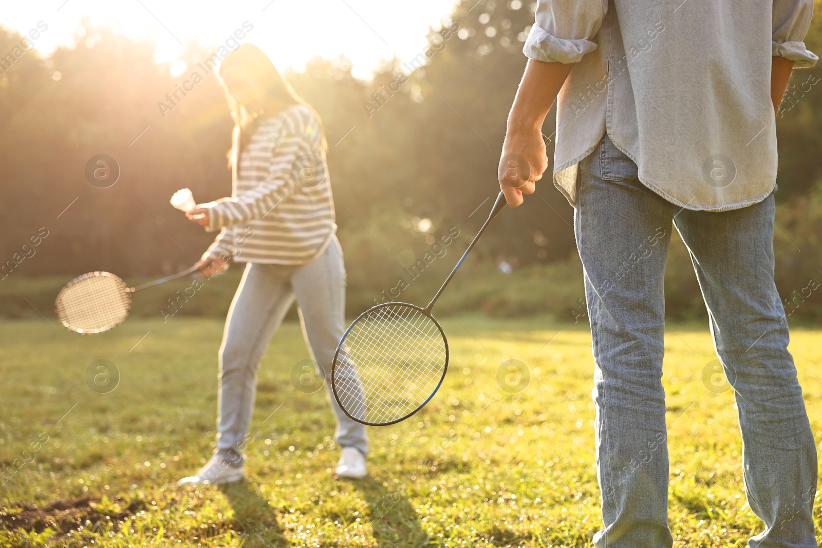 Photo of Young woman and man playing badminton in park on sunny day, selective focus