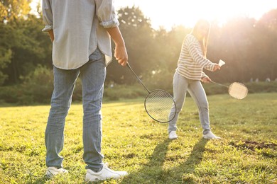 Photo of Young woman and man playing badminton in park on sunny day, selective focus