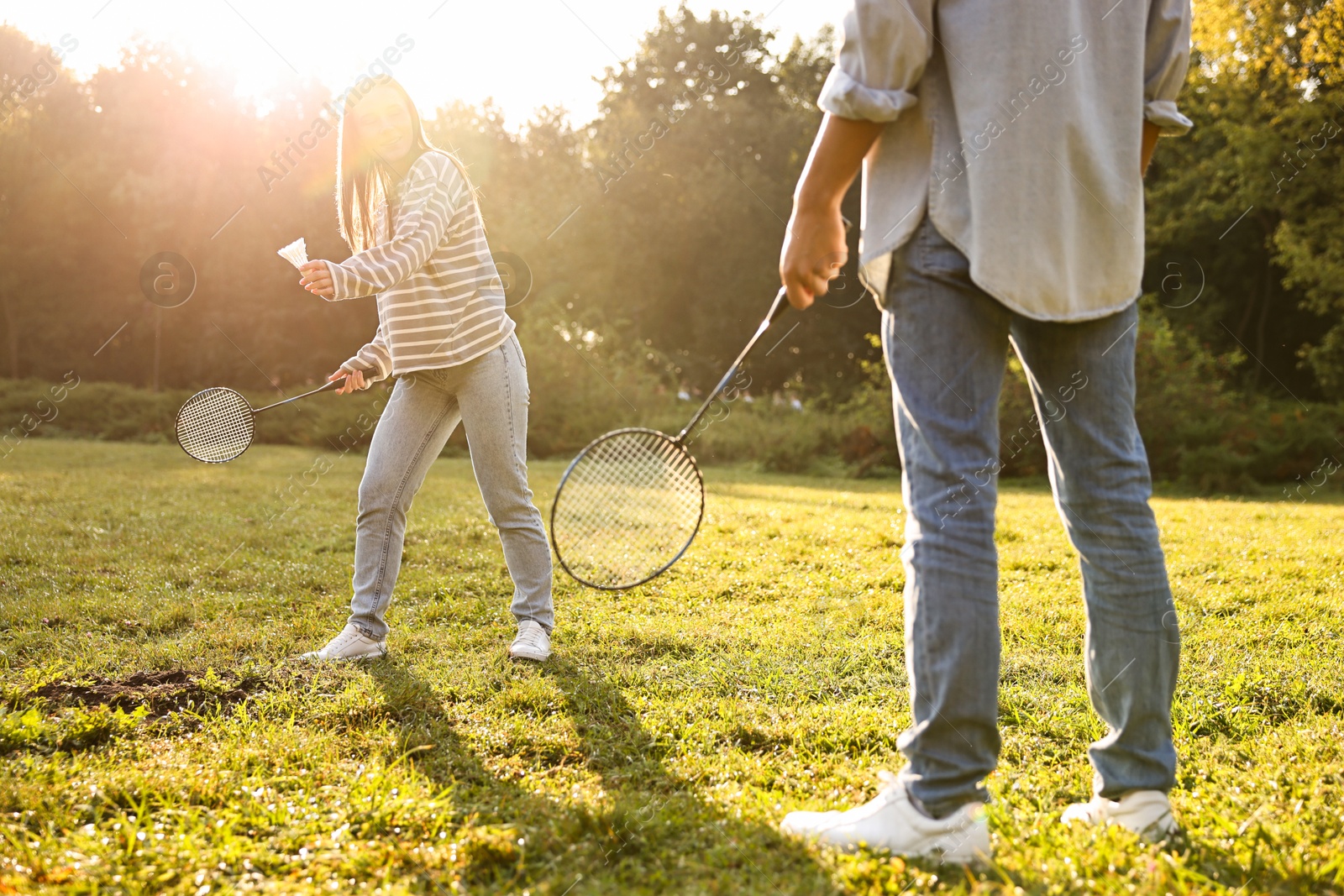 Photo of Young woman and man playing badminton in park on sunny day, selective focus