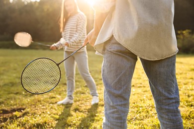 Photo of Young woman and man playing badminton in park on sunny day, selective focus