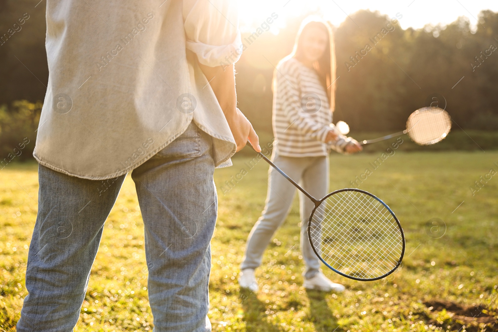 Photo of Young woman and man playing badminton in park on sunny day, selective focus