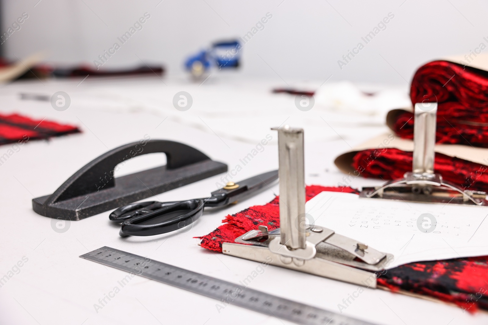 Photo of Pieces of fabric, measurements, scissors and other tools on white table in professional workshop, closeup