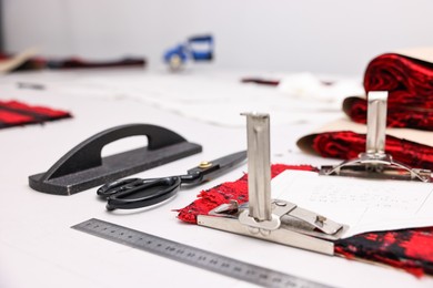 Photo of Pieces of fabric, measurements, scissors and other tools on white table in professional workshop, closeup