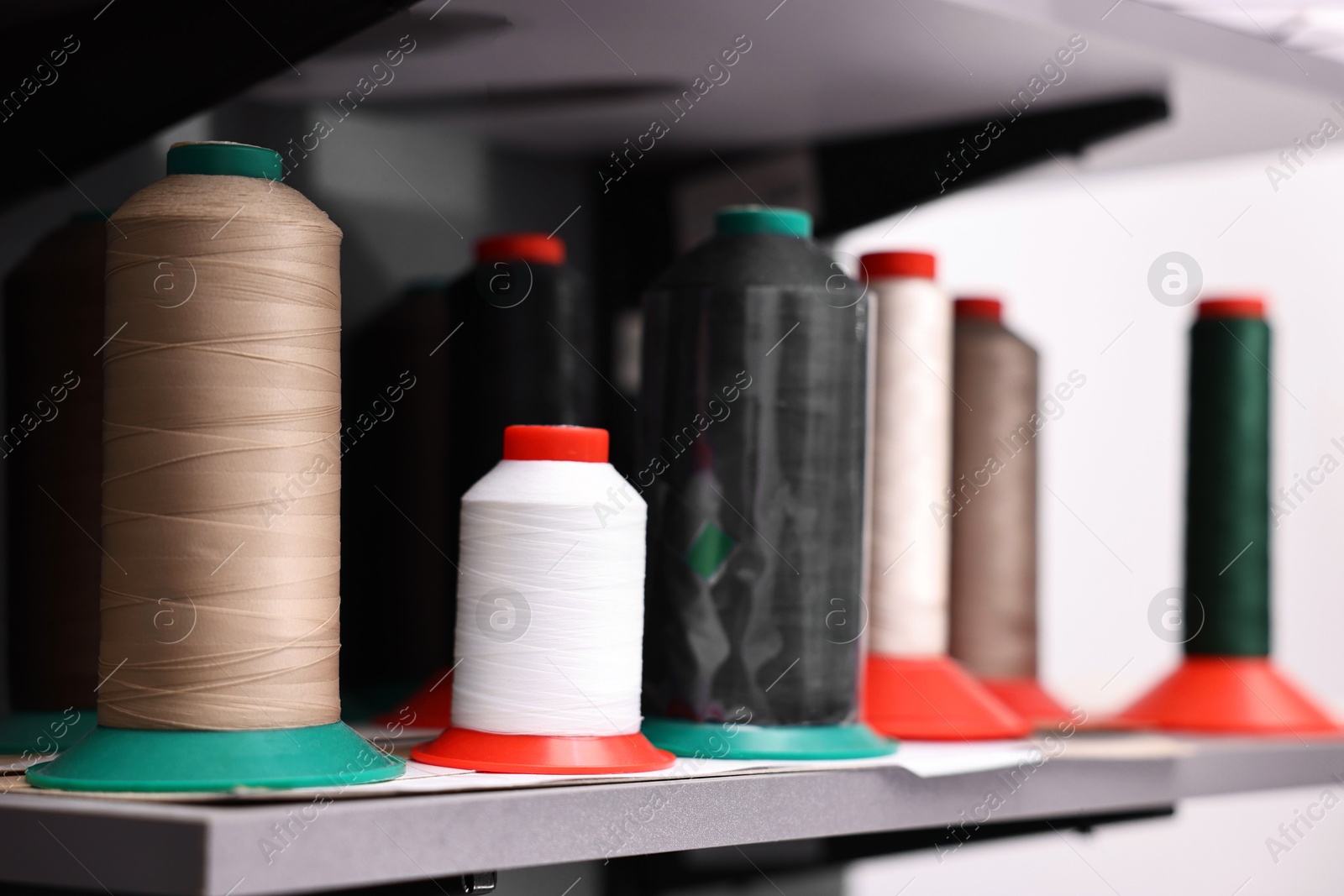 Photo of Many different spools of thread on white shelf in professional workshop