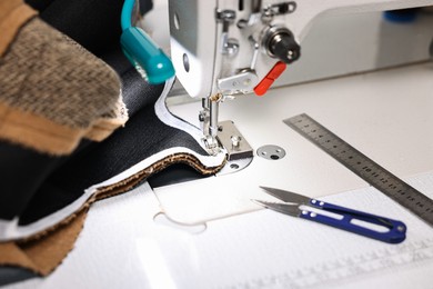 Photo of Sewing machine and other tools on white table in professional workshop, closeup