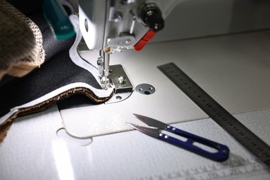 Photo of Sewing machine and other tools on white table in professional workshop, closeup