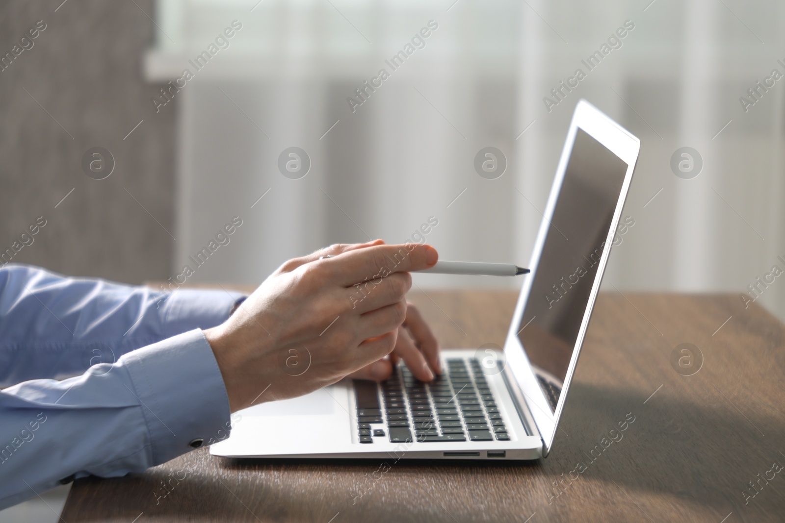 Photo of Businessman using laptop at wooden table indoors, closeup. Modern technology