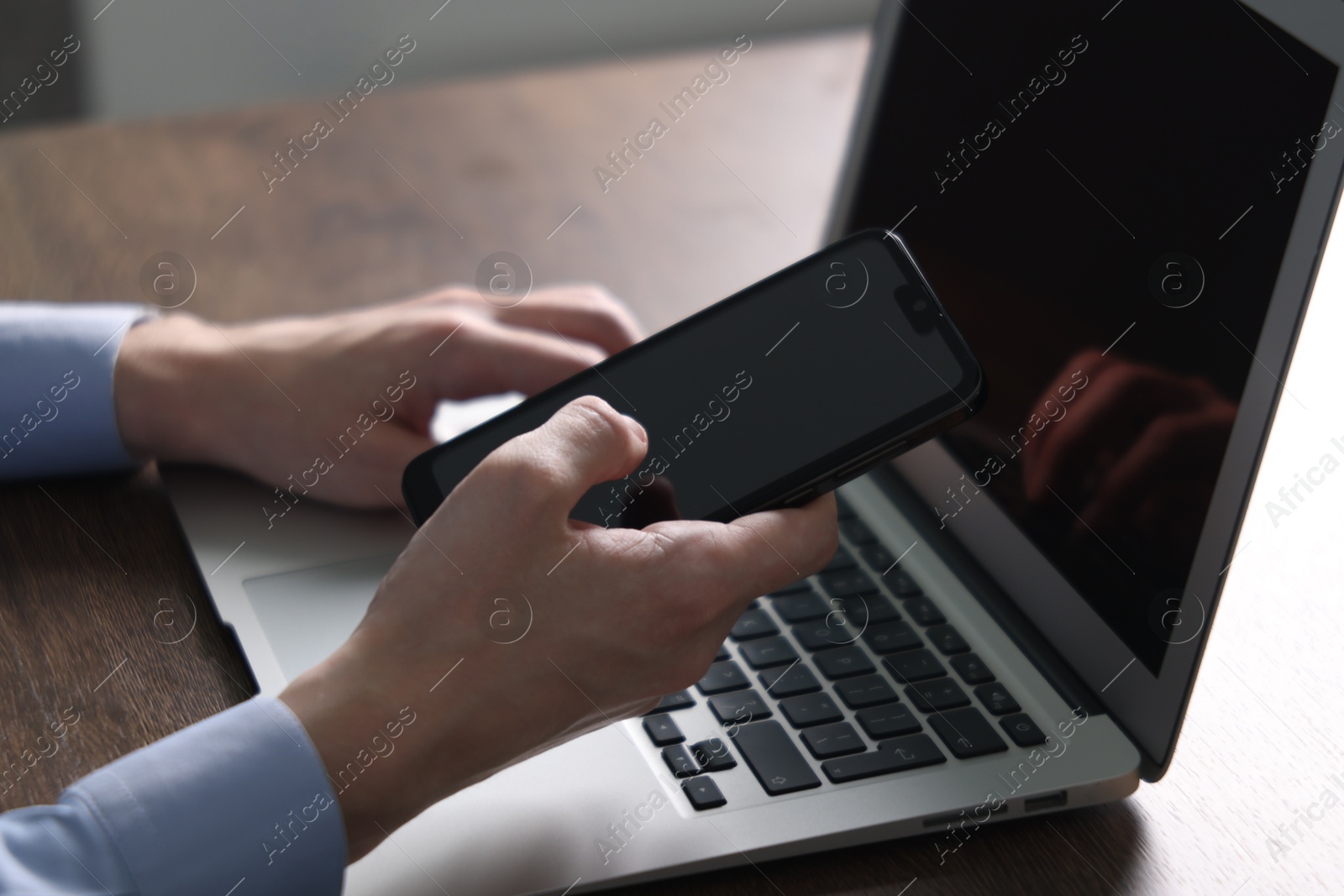 Photo of Businessman using smartphone near laptop at wooden table indoors, closeup. Modern technology