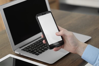 Photo of Businessman using smartphone near laptop and tablet at wooden table indoors, closeup. Modern technology