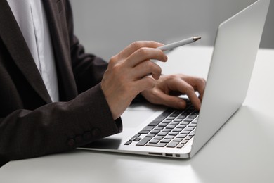 Photo of Businessman using laptop at white table indoors, closeup. Modern technology