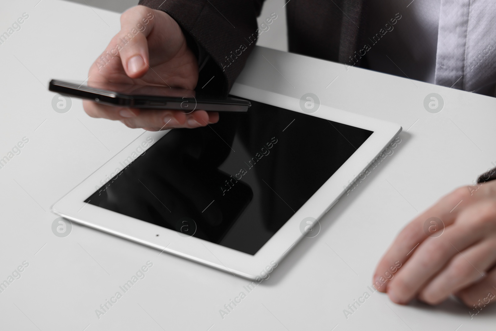 Photo of Businessman using smartphone at white table with tablet, closeup. Modern technology