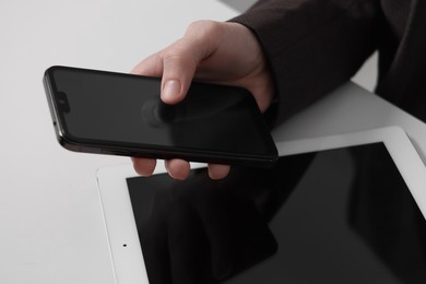 Photo of Businessman using smartphone at white table with tablet, closeup. Modern technology