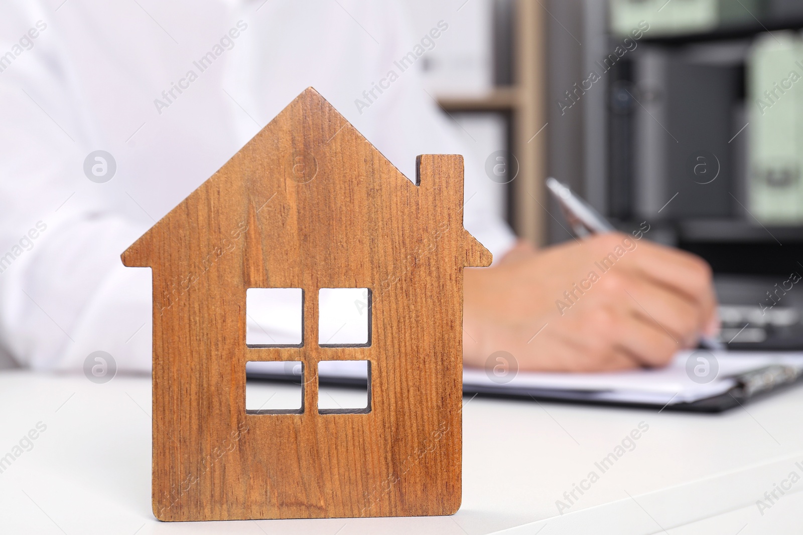 Photo of Real estate insurance. Man writing something at light table, focus on wooden house figure