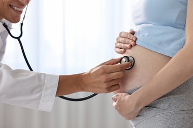 Photo of Pregnancy checkup. Smiling doctor with stethoscope listening baby's heartbeat in patient's tummy indoors, closeup