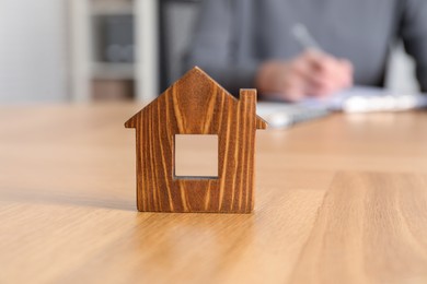 Photo of Property insurance. Real estate agent working at table indoors, focus on wooden house figure