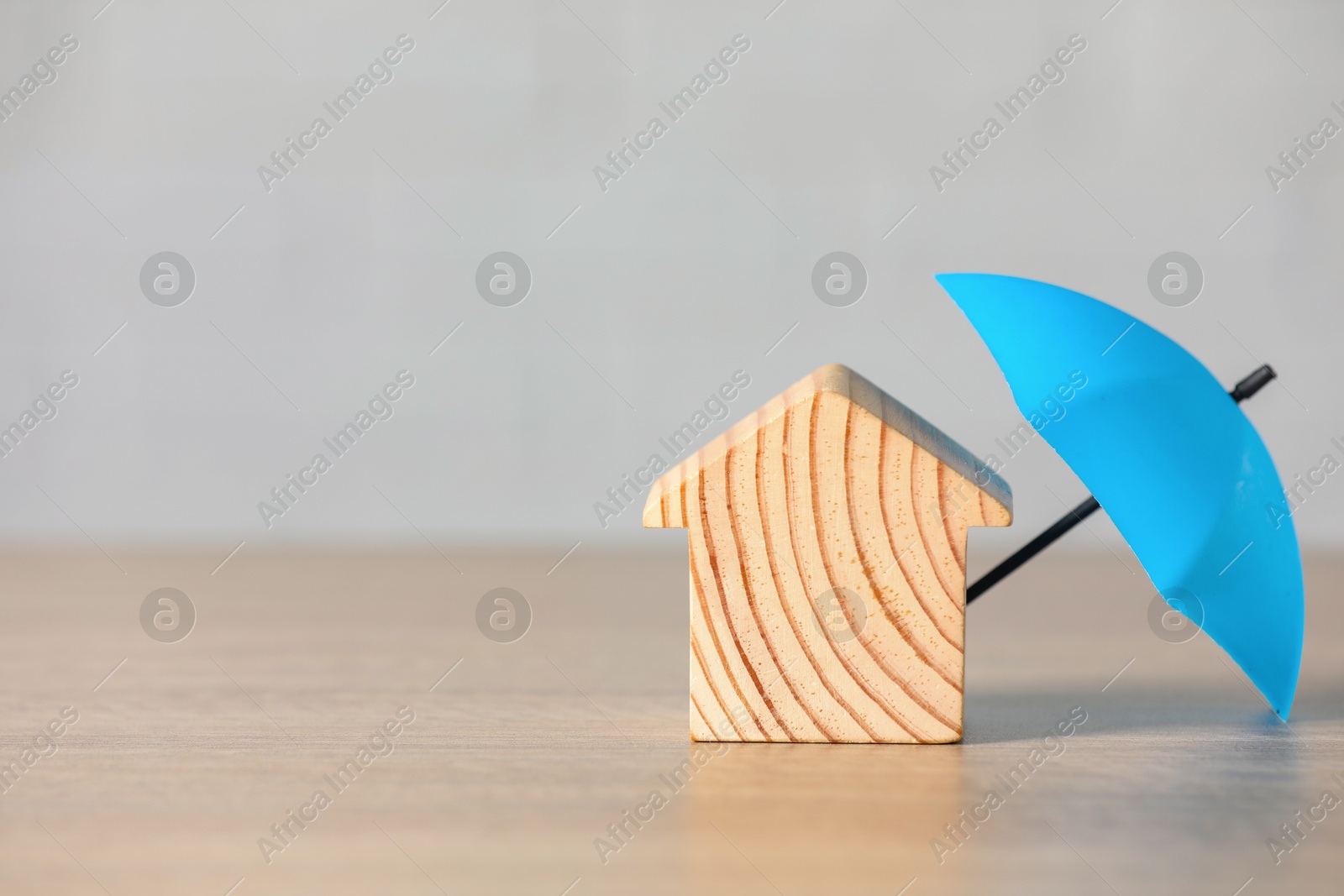 Photo of Property insurance. Wooden house figure and small umbrella on table, space for text