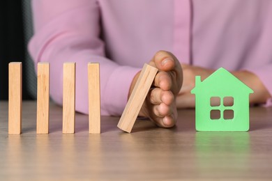 Photo of Property insurance. Real estate agent protecting house figure at wooden table indoors, closeup