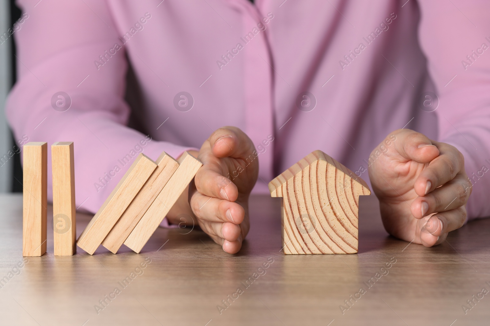 Photo of Property insurance. Real estate agent protecting wooden house figure at table indoors, closeup