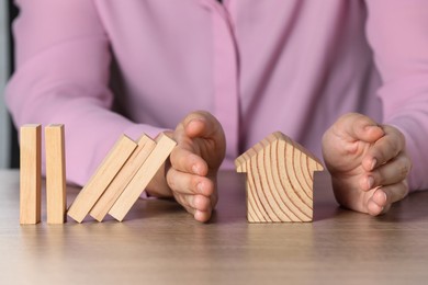 Photo of Property insurance. Real estate agent protecting wooden house figure at table indoors, closeup