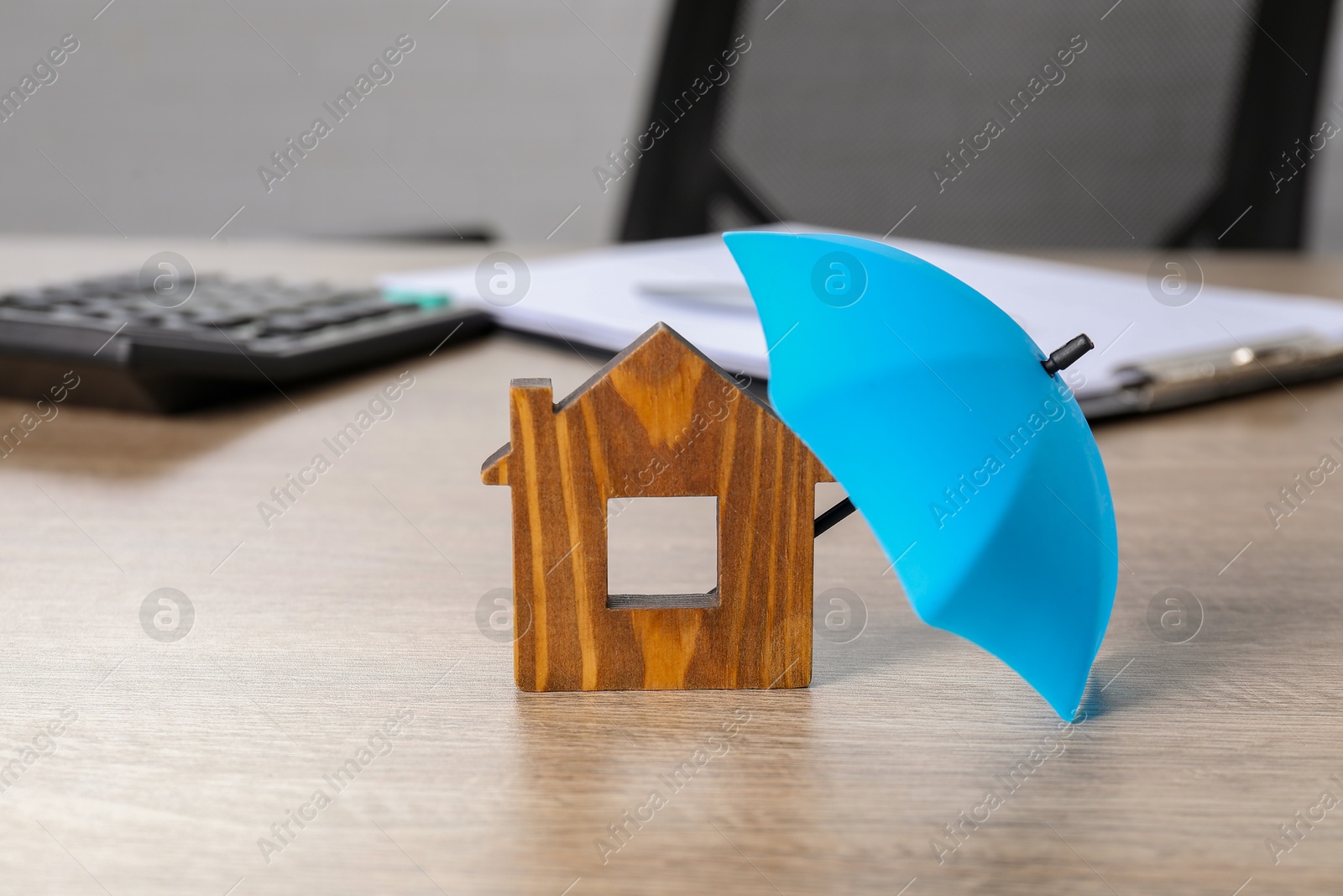 Photo of Property insurance. Wooden house figure and small umbrella on table indoors