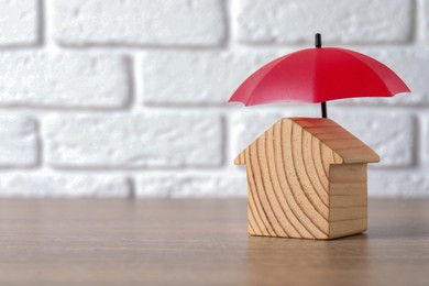 Photo of Property insurance. Wooden house figure and small umbrella on table indoors, space for text