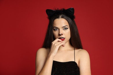 Photo of Beautiful woman with cat makeup and ears on red background