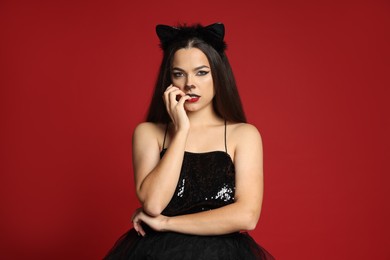 Photo of Woman with cat makeup and ears in beautiful dress on red background