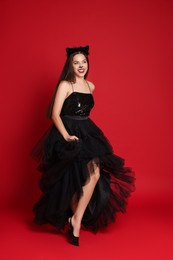 Photo of Woman with cat makeup and ears in beautiful dress on red background