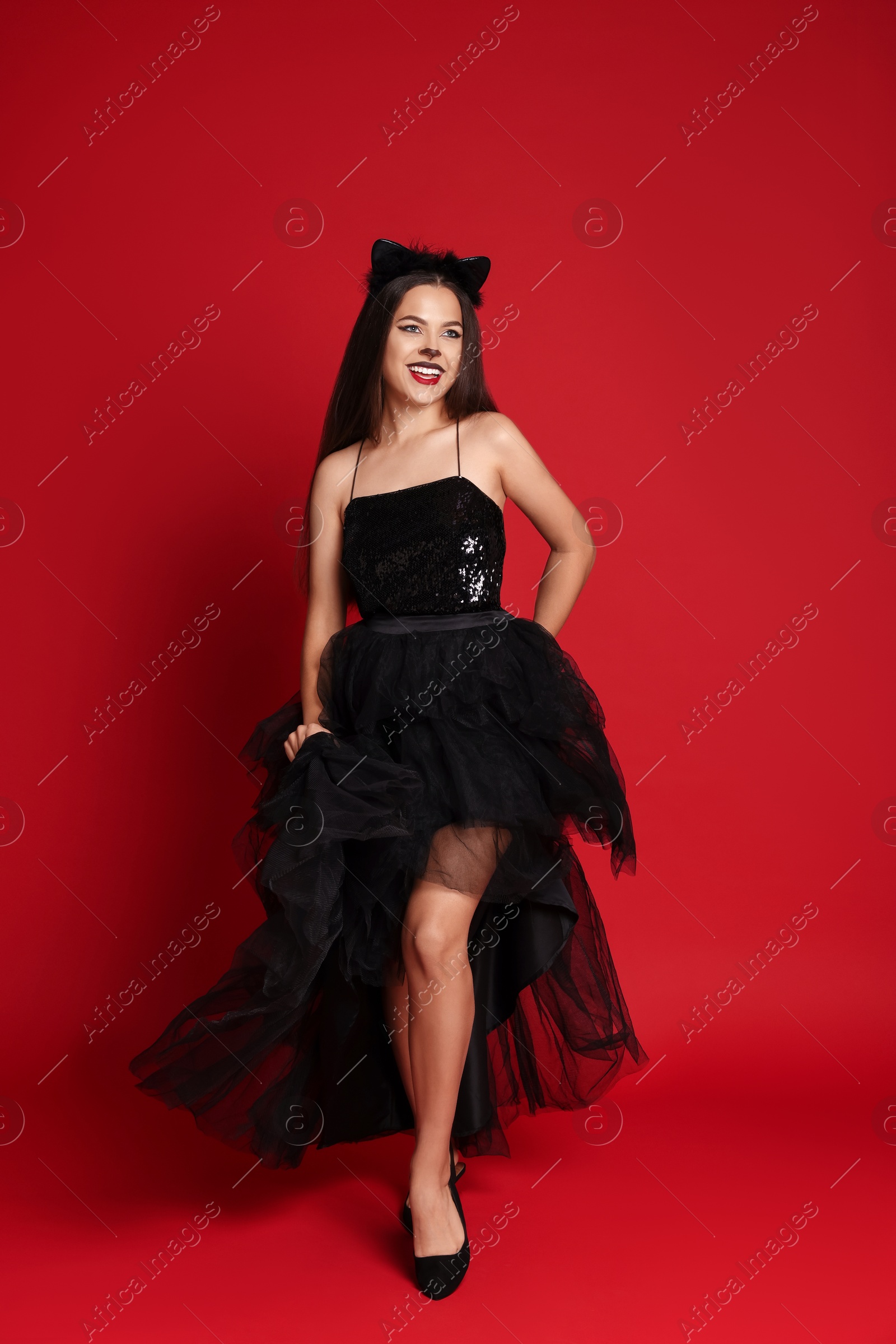 Photo of Woman with cat makeup and ears in beautiful dress on red background