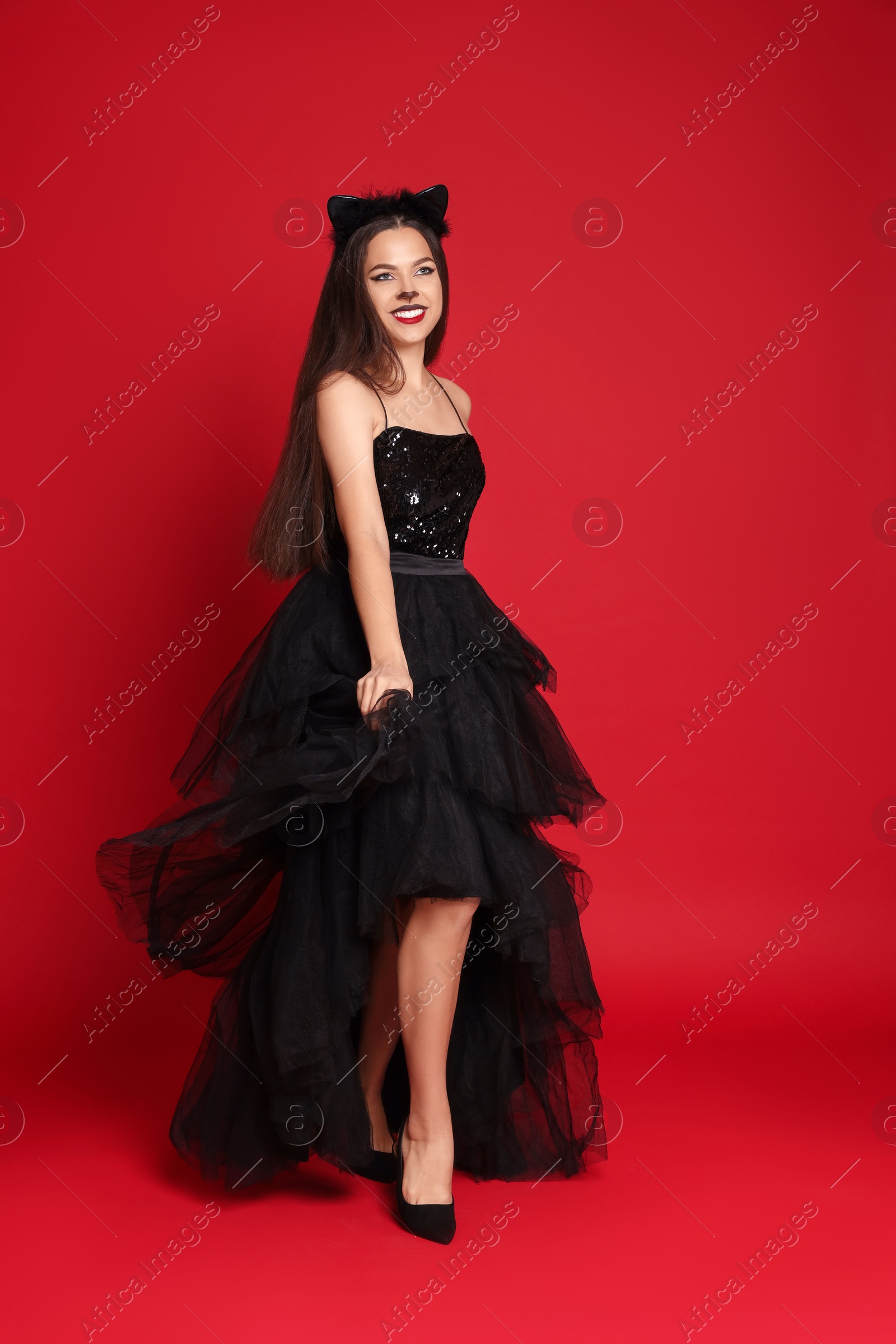 Photo of Woman with cat makeup and ears in beautiful dress on red background