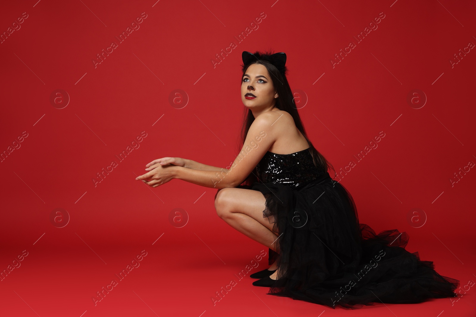 Photo of Woman with cat makeup and ears in beautiful dress on red background. Space for text