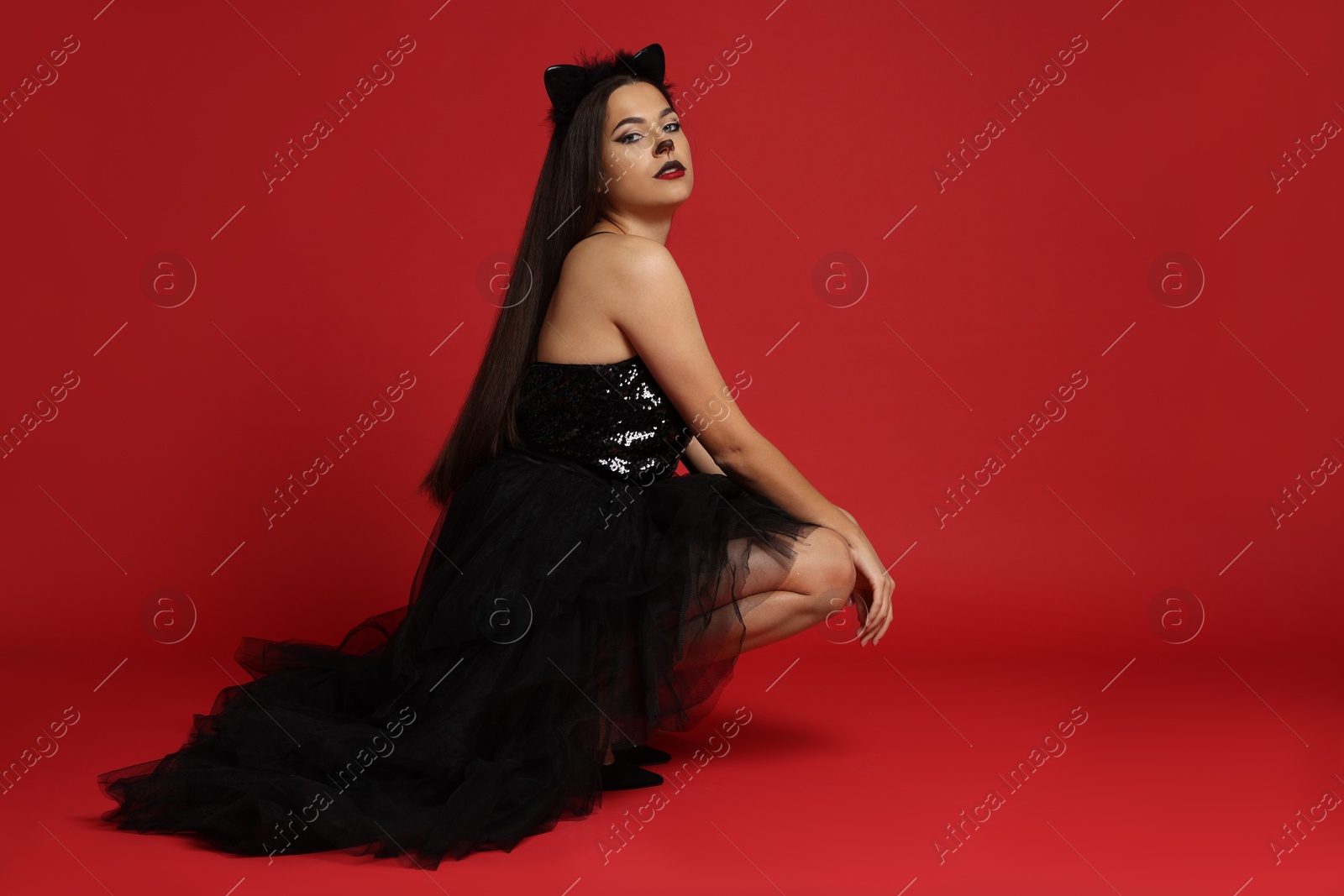 Photo of Woman with cat makeup and ears in beautiful dress on red background. Space for text