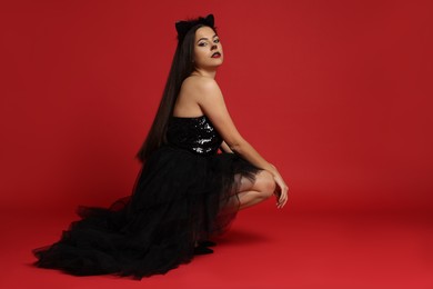 Photo of Woman with cat makeup and ears in beautiful dress on red background. Space for text