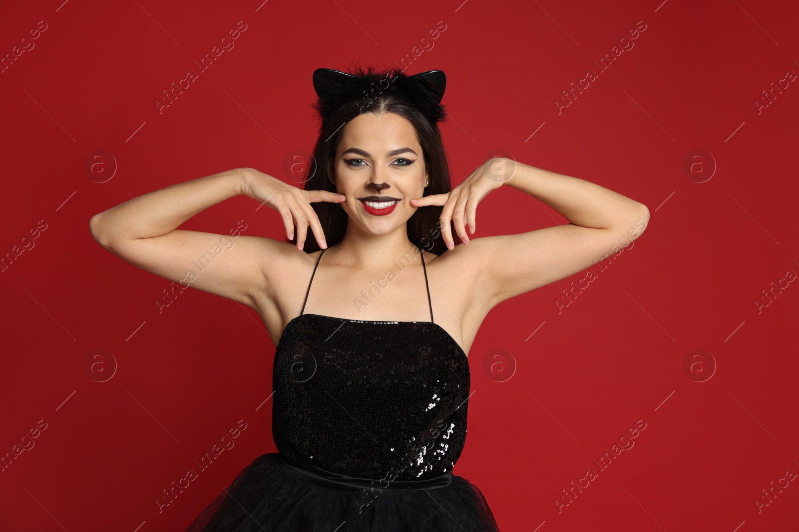 Photo of Woman with cat makeup and ears in beautiful dress on red background