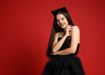 Photo of Woman with cat makeup and ears in beautiful dress on red background. Space for text