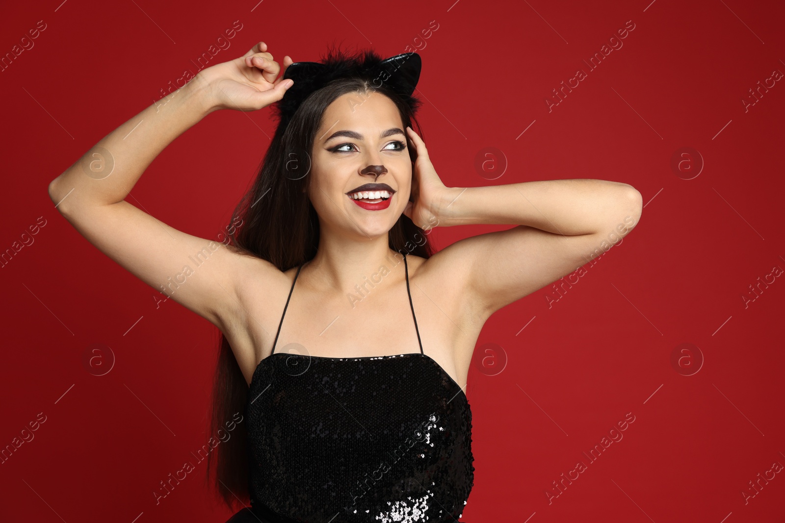 Photo of Beautiful woman with cat makeup and ears on red background