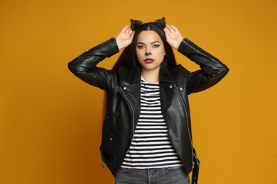 Photo of Woman with cat makeup and ears in leather jacket on orange background