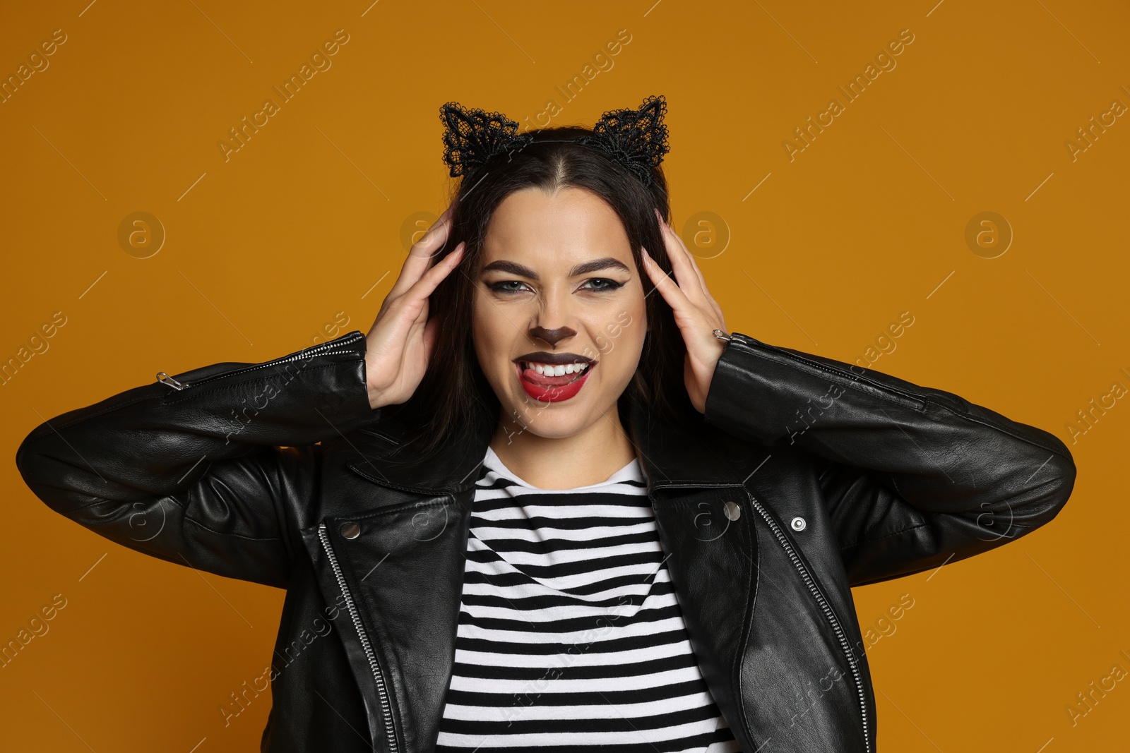 Photo of Woman with cat makeup and ears in leather jacket on orange background