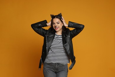 Photo of Woman with cat makeup and ears in leather jacket on orange background