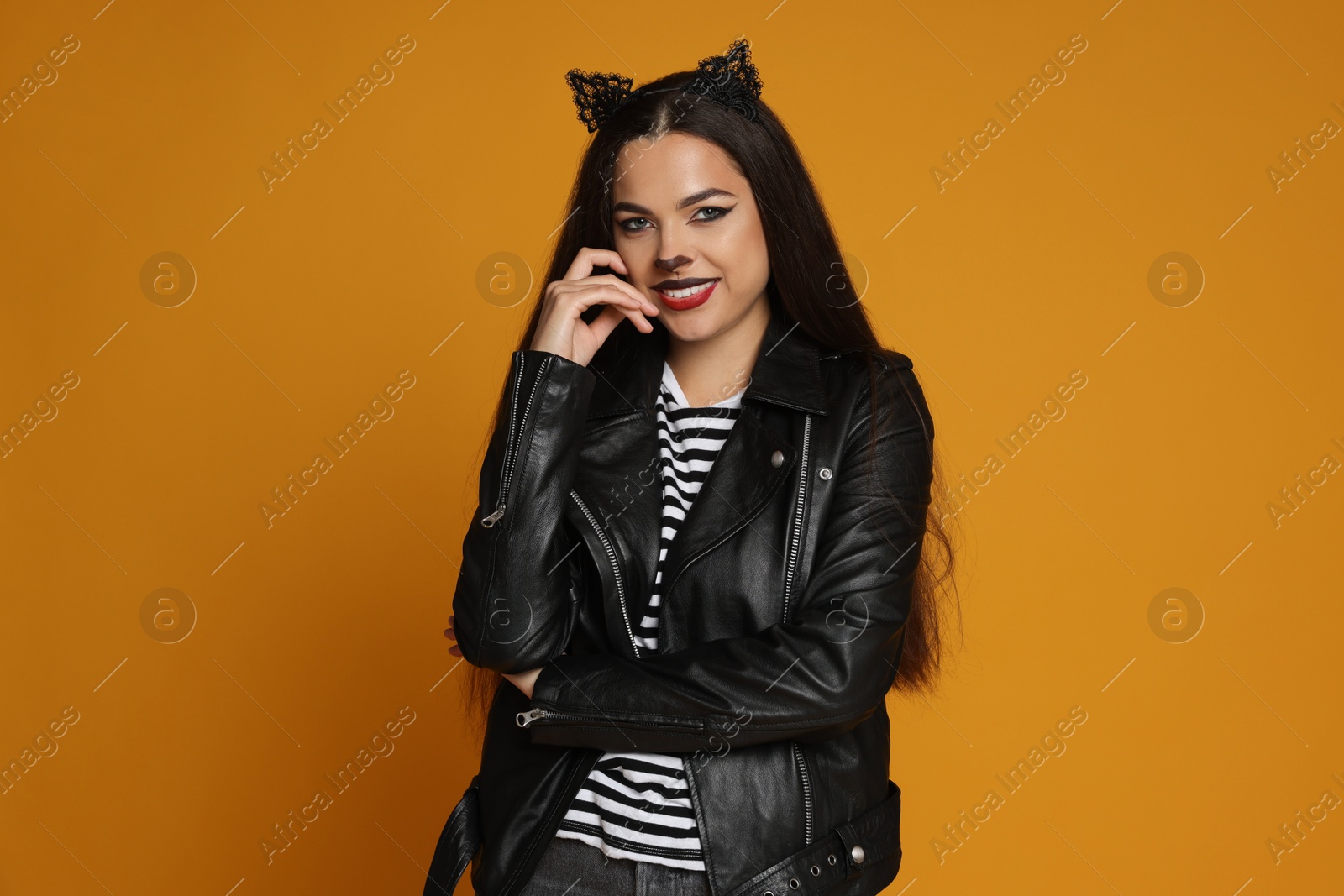 Photo of Woman with cat makeup and ears in leather jacket on orange background