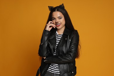 Photo of Woman with cat makeup and ears in leather jacket on orange background