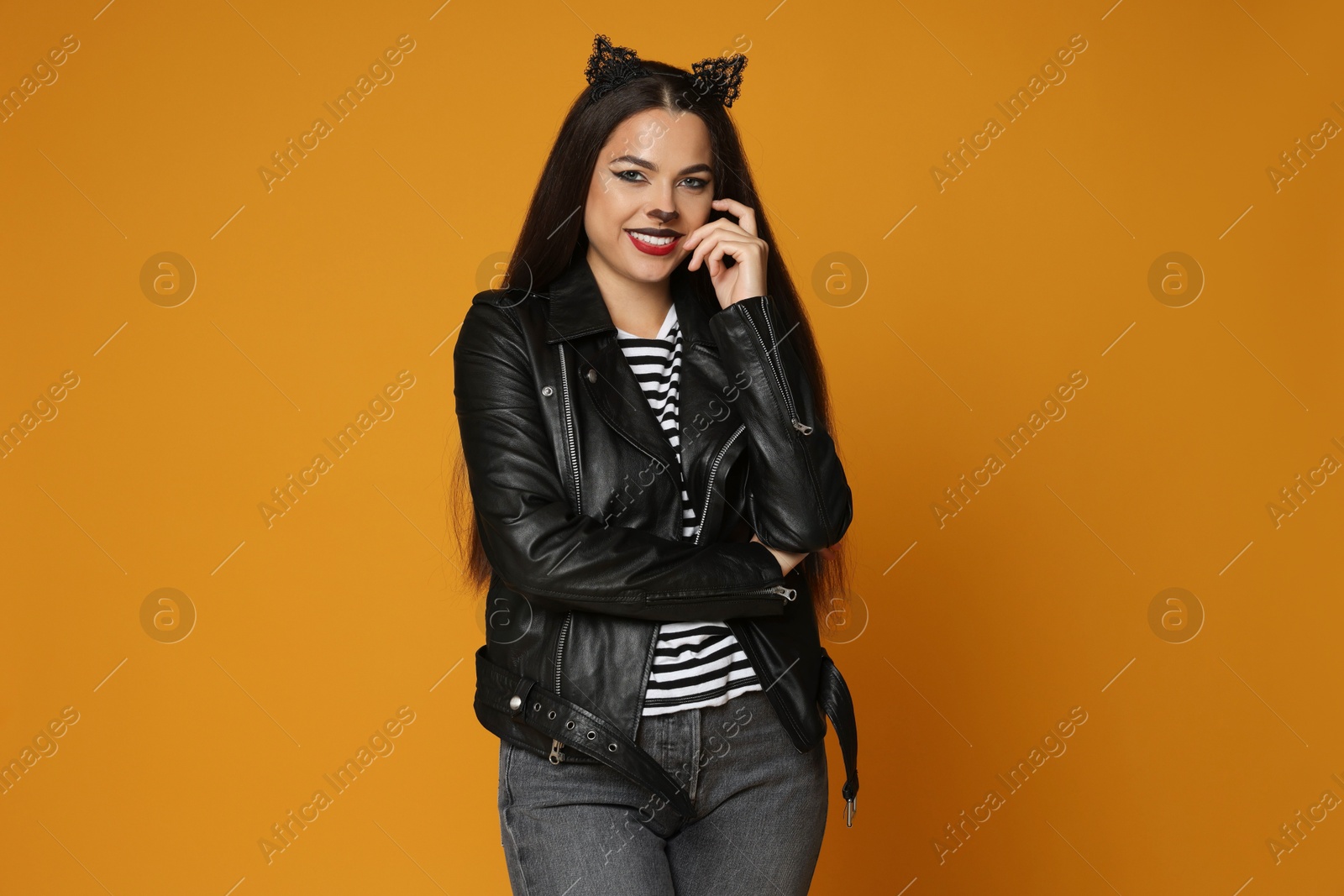 Photo of Woman with cat makeup and ears in leather jacket on orange background