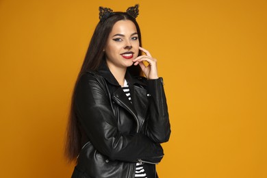 Photo of Woman with cat makeup and ears in leather jacket on orange background