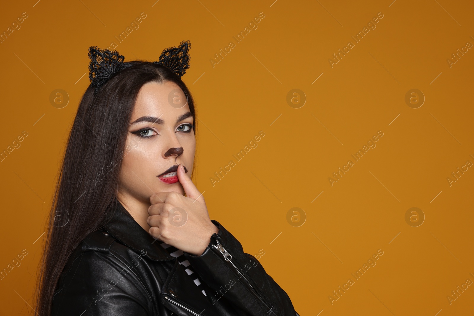 Photo of Woman with cat makeup and ears in leather jacket on orange background. Space for text