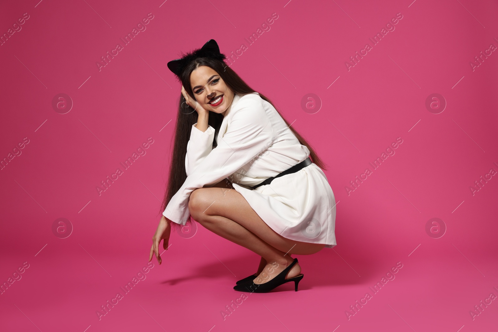 Photo of Charming woman with cat makeup and ears in stylish outfit on pink background