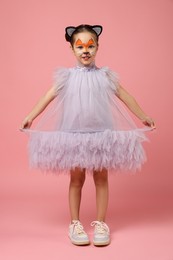 Photo of Cute girl with painted face and ears as cat on pink background