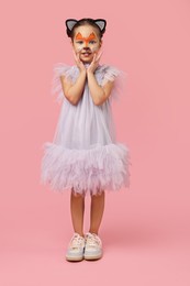 Photo of Cute girl with painted face and ears as cat on pink background