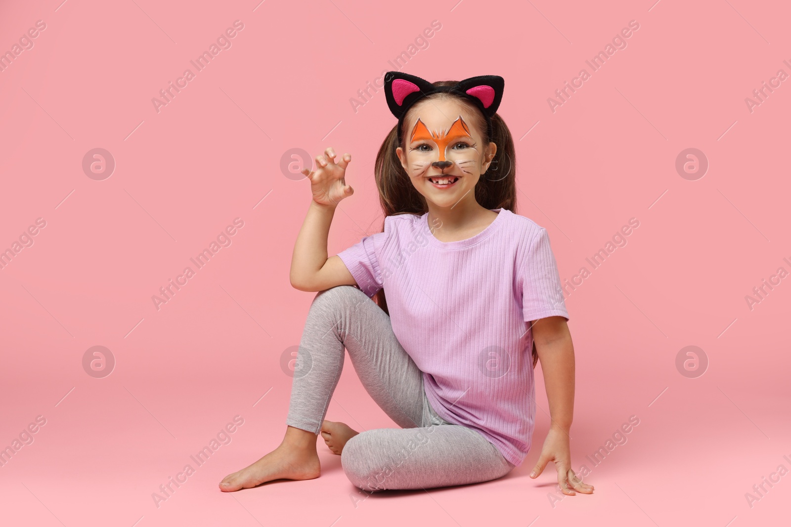 Photo of Cute girl with painted face and ears as cat on pink background