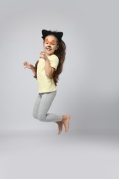 Photo of Cute girl with painted face and ears as cat jumping on grey background, space for text